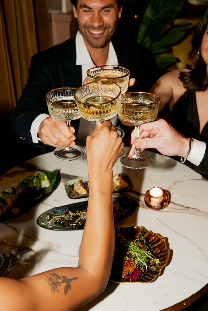 Gasten proosten met vergulde coupes boven een tafel met hapjes bij Bar Santé